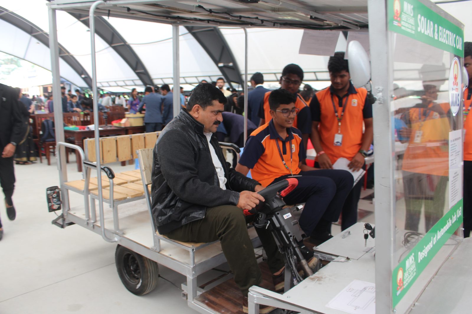 MMS staff driving the Solar and Electric Car at Alliance NOVA Fest, with a student assisting at the wheel