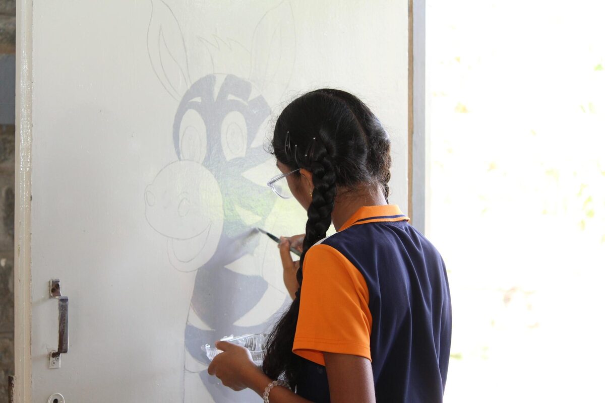 A student sketching a design on a wall as part of a mural project