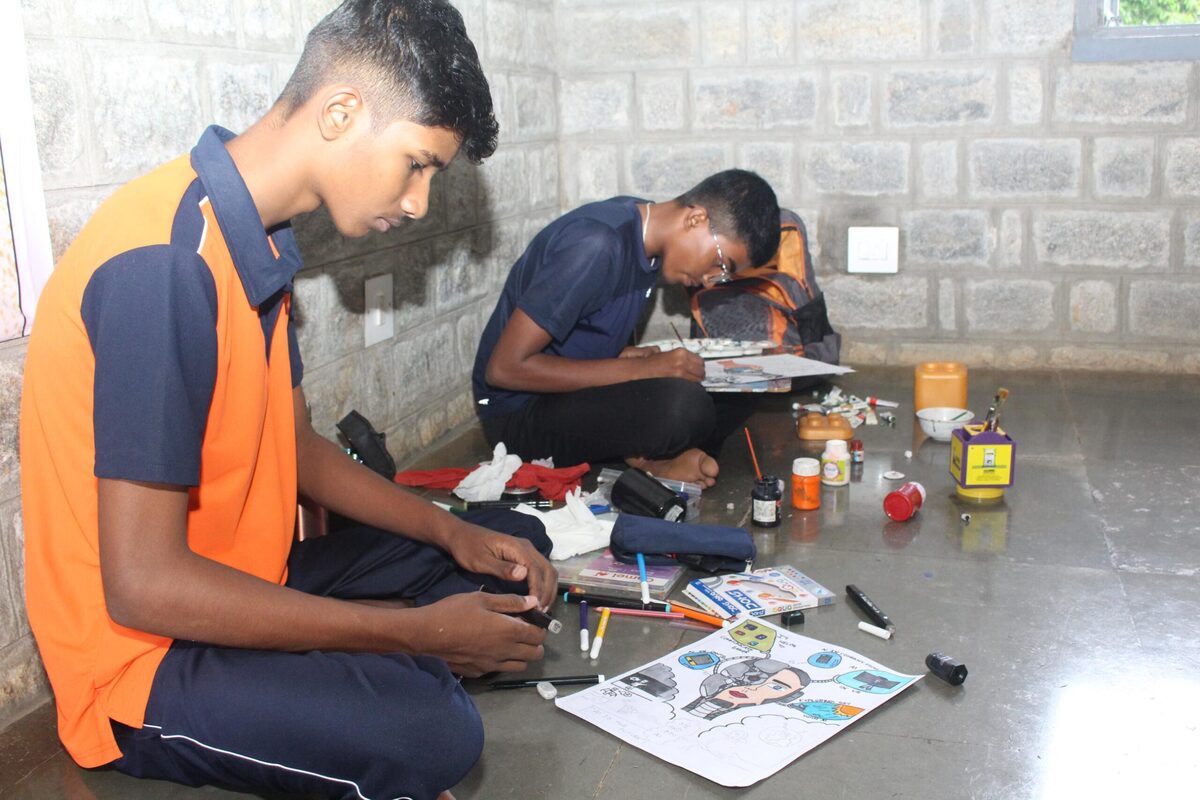 A student adding finishing touches to his artwork with paints nearby