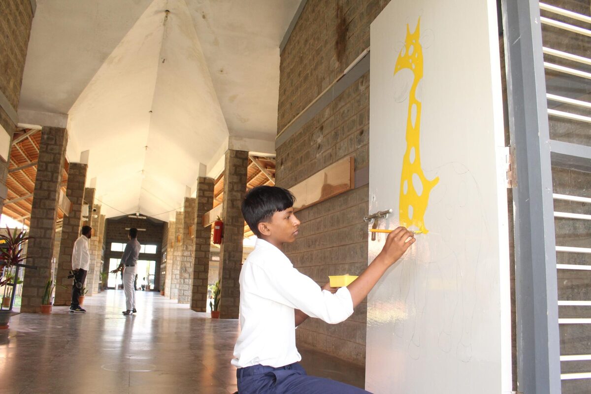A student painting a mural design on a pillar in the school corridor