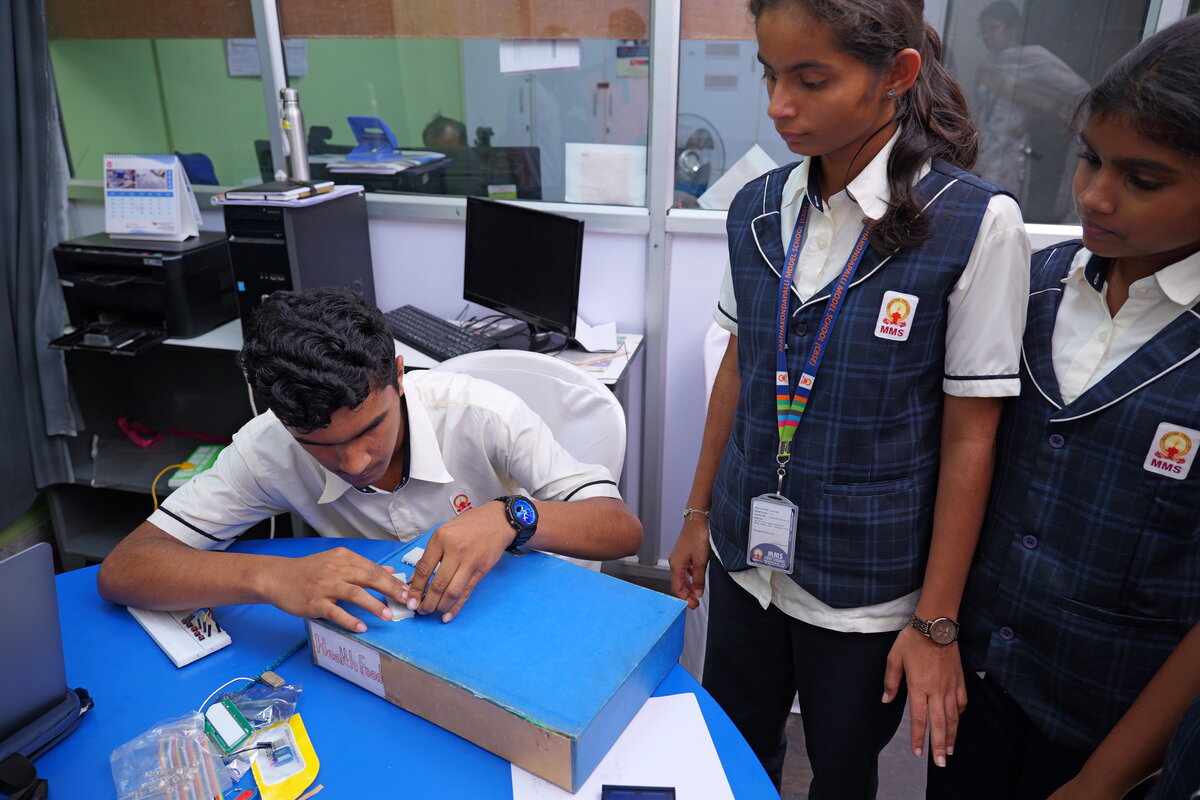 A student wiring a switch into a prototype enclosure while classmates watch