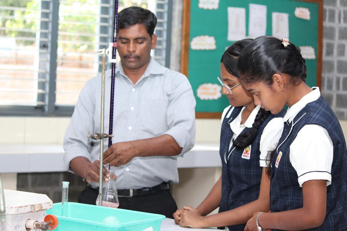 Staff guiding students through a titration experiment at the chemistry workbench