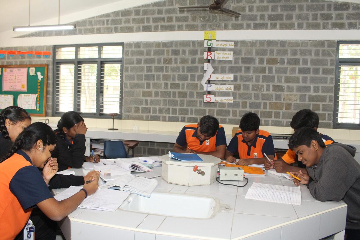 Students recording readings from an ammeter-voltmeter circuit, guided by staff