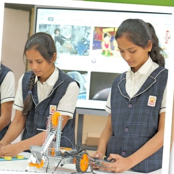 Students building a robotics kit with a screen displaying reference material behind them