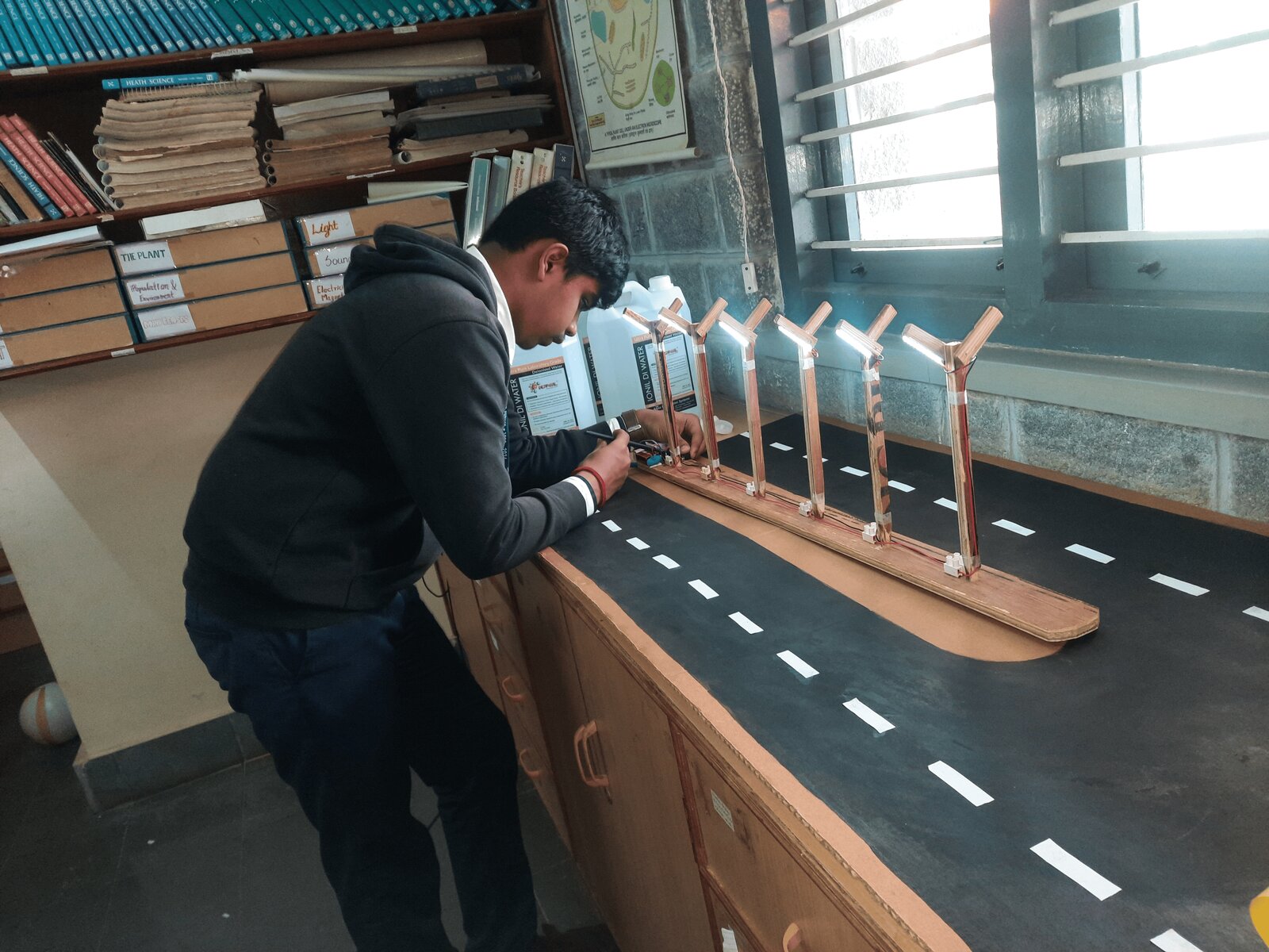 A student wiring and testing a row of five lit LED highway signal posts on the model road