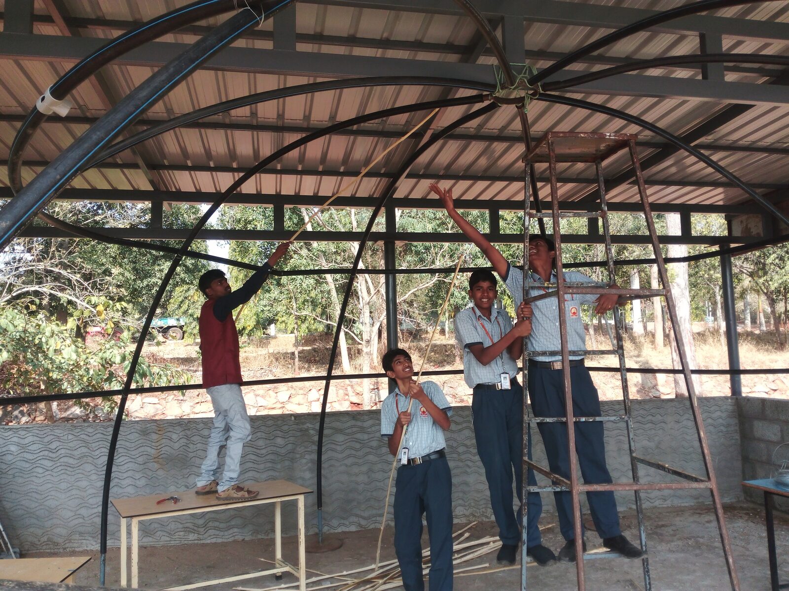 Students smiling while tying bamboo splines to the dome frame near its apex