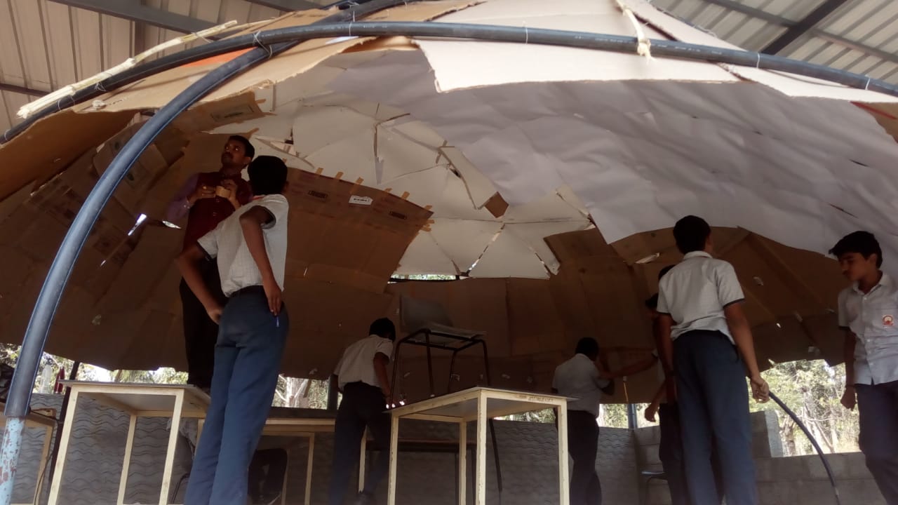 Students and a teacher inside the dome taping the cardboard ceiling panels together from below
