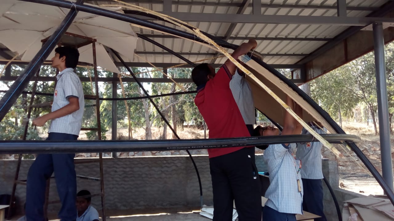 Students fitting cardboard panels along the curved ribs of the dome