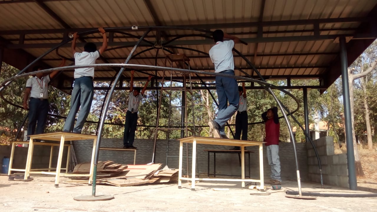 Students fitting more curved ribs into the planetarium dome frame while standing on desks