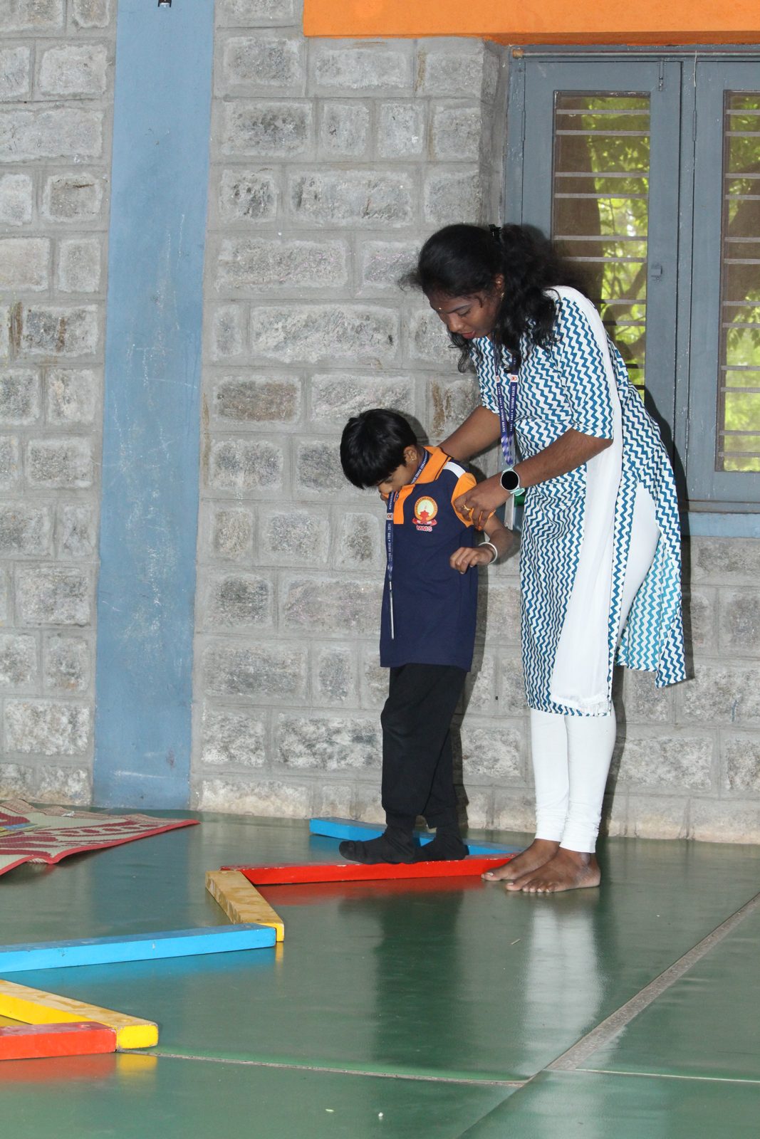 A child walking along a low balance beam with an educator holding the child's hands