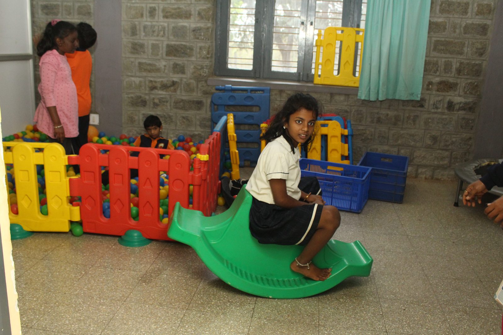 A girl on a green rocker in a play zone with soft play fencing