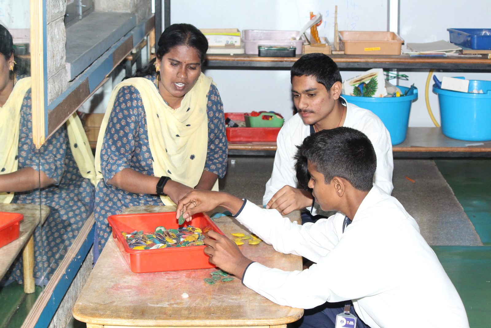An educator and a student sorting colourful beads in a red tray
