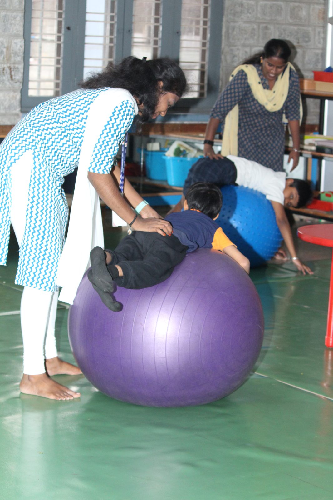 An educator supporting a child on a large therapy ball
