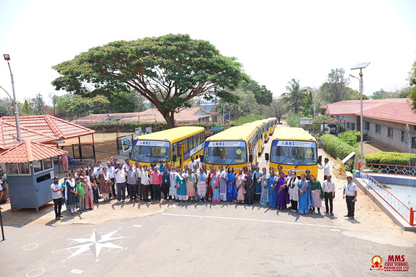 Staff and team members gathered in front of the line of school buses at the campus gate
