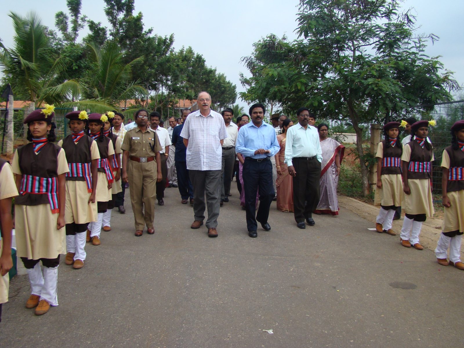 Guests walking along the campus road between two lines of students in uniform forming a guard of honour